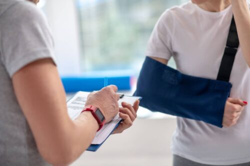 A woman with her arm in a sling describes her slip and fall accident to a nurse who takes notes.