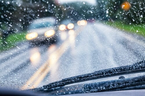 First-person perspective of a driver navigating the road during a rainstorm. Rain on the windshield has obscured the drivers on the other side of the road.
