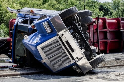 A blue and red semi truck overturned on the side of the road after an accident.